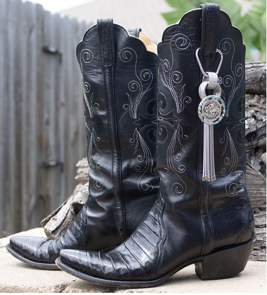 Pair of worn black cowboy boots with a decorative keychain.