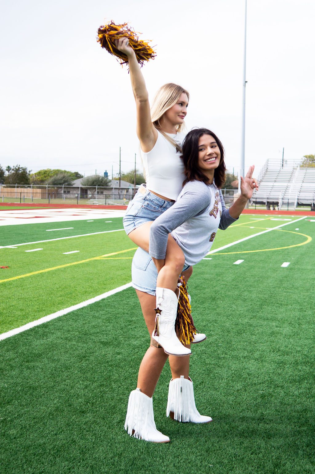 Two cheerleaders posing on a football field.