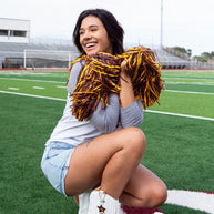 Cheerleader kneeling on football field, smiling.